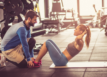 trainer helping a woman doing curl ups