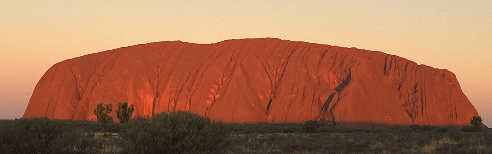 Uluru / Ayers Rock glowing red at sunset against a desert sky in the Northern Territory