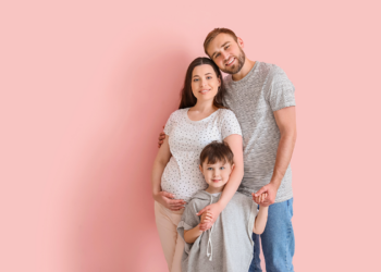 Pregnant mother, father, and son poses for a photo on a pink backgroun