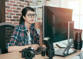 Female photographer holding a cup of coffee while working on a computer