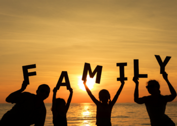 Family holding a cardboard cutout of the word "Family" during a sunset